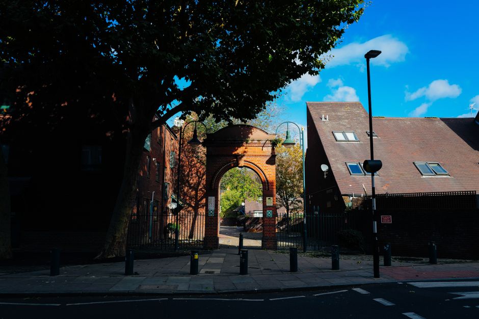 A man with a beard, wearing a white polo shirt and sunglasses, is seen loading or unloading cardboard boxes from the back of a van parked on a residential street during sunset. The van's interior is v